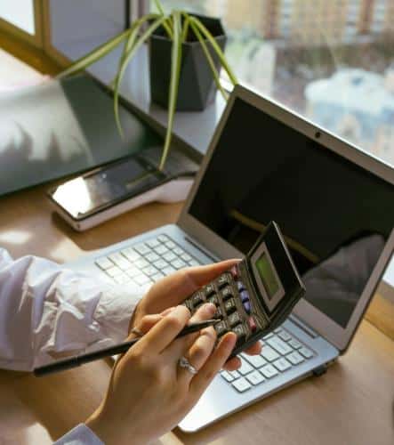 Comptabilité et gestion de budget avec une calculatrice Une personne utilise une calculatrice et un stylo devant un ordinateur portable pour gérer son budget au bureau.